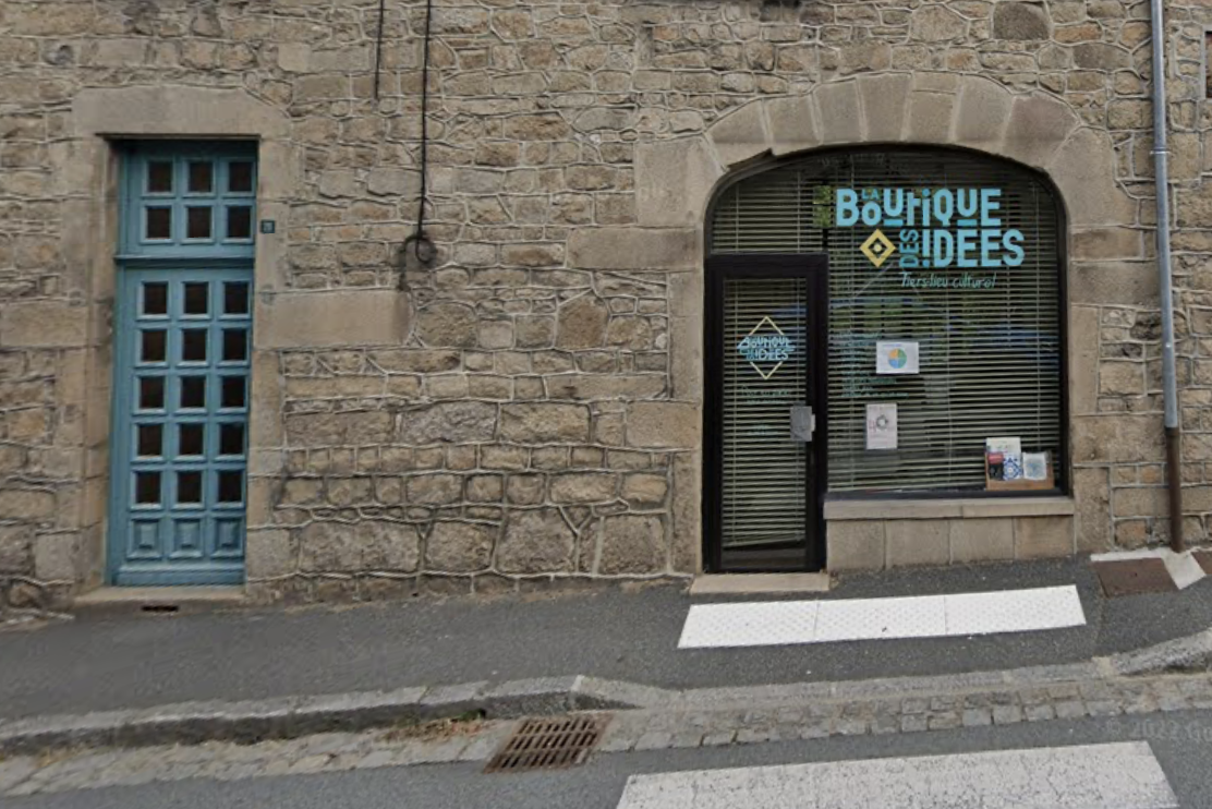 Rez-de-chaussée d'une maison en pierre. Le mur est percé à droite d'une vitrine avec une porte sur lesquelles est inscrit en Bleu ciel et sur deux lignes : "LA BOUTIQUE DES IDÉES". À gauche une porte en bois peinte du même bleu et percée de petits carreaux de verre.